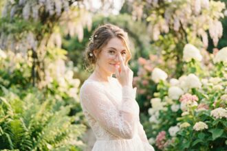 Mariée souriante portant des lunettes à monture fine dorée rose dans un jardin botanique le jour de son mariage